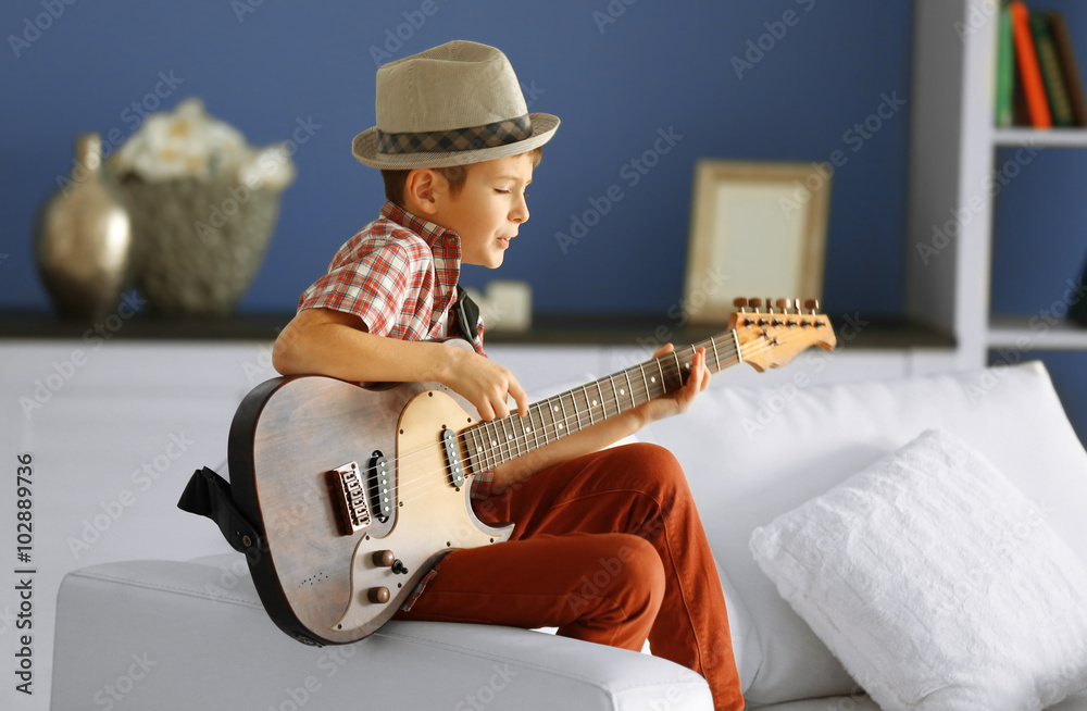 Little boy playing guitar ans singing on a sofa at home