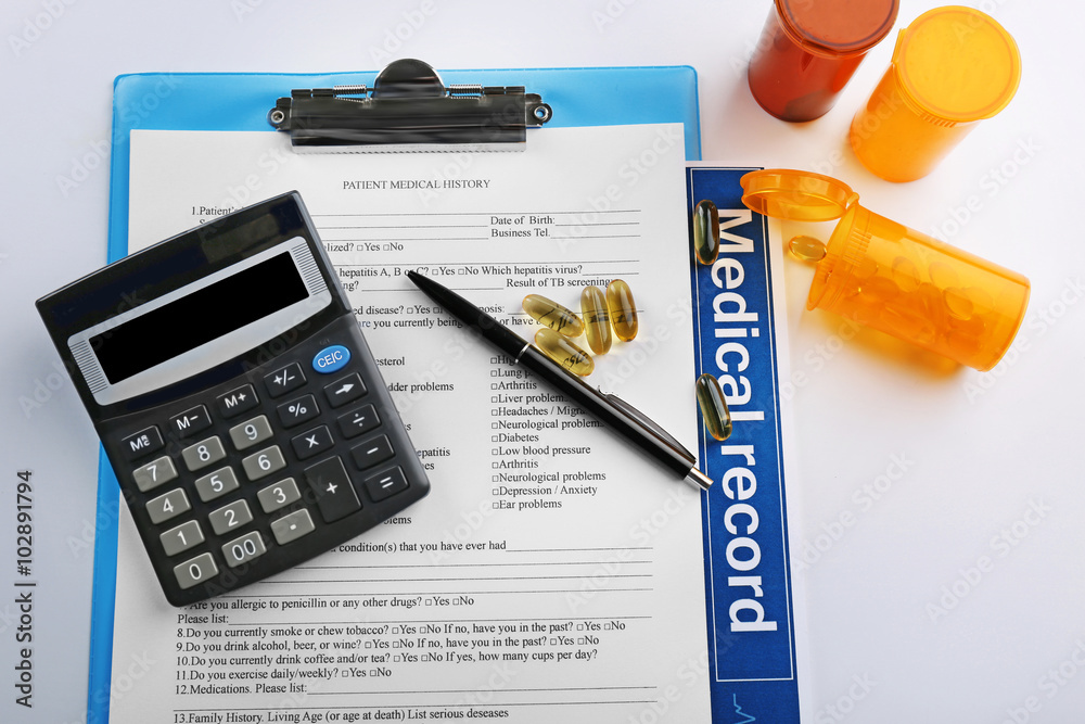 A stethoscope, pills, pen, calculator and clipboard, close-up