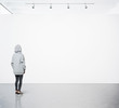 © SFIO CRACHO - Young woman walking in modern gallery and looking at the blank canvas. Square