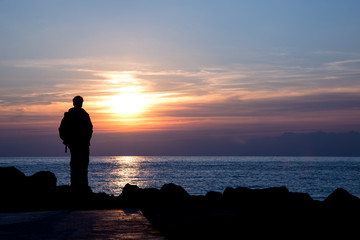 Silhouette of a man admiring winter sunset over italian sea - negative space on the right