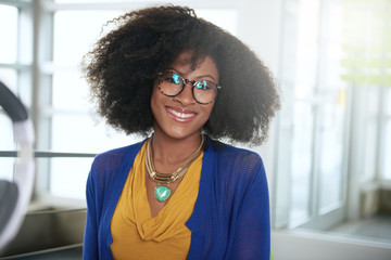 Wall Mural - Portrait of a smiling woman with an afro at the computer in bright glass office