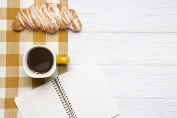 Cup of coffee with fresh croissant and paper notes on wooden bac