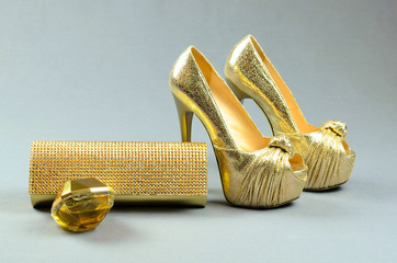 Gold high-heeled shoes, clutch bag and perfume on a gray  backgr