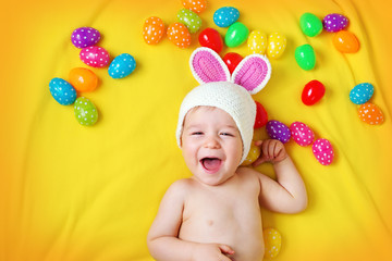 Wall Mural - Baby boy in bunny hat lying on yellow blanket with easter eggs