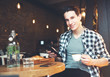 © Tijana - Young man sitting at a cafe, using a tablet, drinking espresso