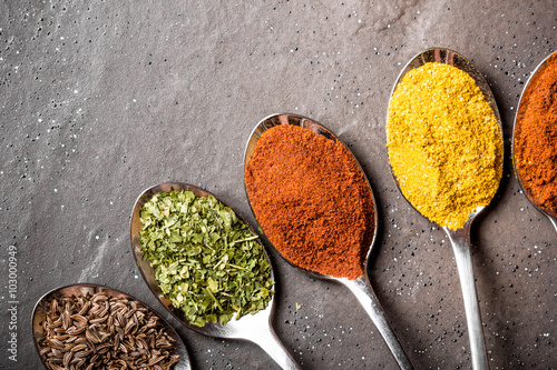 Naklejka na szybę Colorful spices on metal spoons on black rough rock surface.