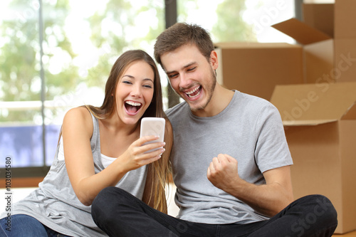 Fotografía Euphoric couple moving house and watching phone