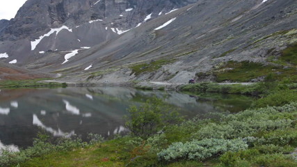 Wall Mural - Quad bike driving on the mountain road near tranquil beautiful lake with reflection. Khibiny massif, Kolsky peninsula, Russia