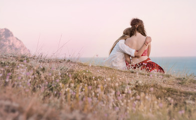 Two Hippie friends in field on sunset, Blue sea and sky on background. 