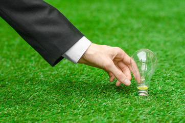 Electricity and business theme: a man in a black suit holding a light bulb against a background of green grass