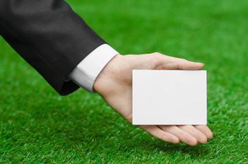 Discounts and business topic: hand in a black suit holding a white blank card on green grass background