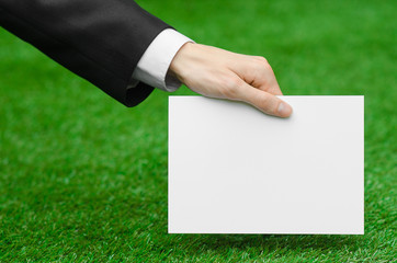 Discounts and business topic: hand in a black suit holding a white blank card on green grass background