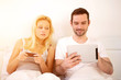 © Production Perig - Young attractive couple using mobile and tablet in bed