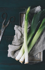 Wall Mural - Leek and scissors on a light textile and metal plate on a dark background of the aged wooden boards vintage vertical top view