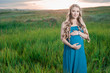 Beautiful tender pregnant woman standing on green grass and looking at the camera