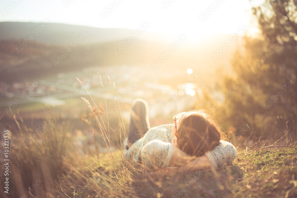 arefree happy woman lying on green grass meadow on top of mountain edge cliff enjoying sun on her face.Enjoying nature sunset.Freedom.Enjoyment.Relaxing in mountains at sunrise.Sunshine.Daydreaming - obrazy, fototapety, plakaty 