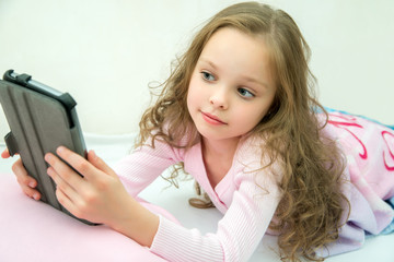 happy little girl lying on bed with tablet computer