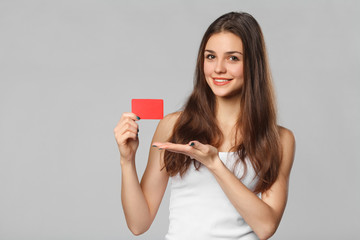 Smiling woman showing blank credit card in white t-shirt, isolated over gray background