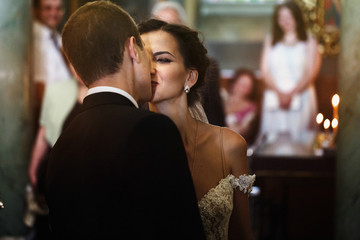 happy smiling brunette bride kissing groom in black suit in chur