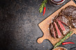 Sliced medium rare grilled steak on rustic cutting board with rosemary and spices , dark rustic metal background, top view, place for text