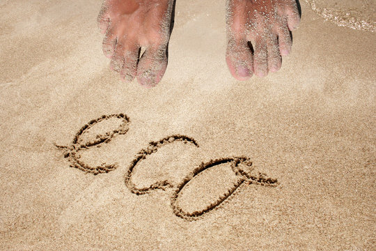 Concept or conceptual eco text handwritten in sand on a beach in an exotic island background