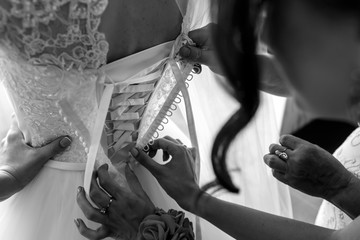 Bridesmaids help put on & tie corset on wedding dress closeup b&