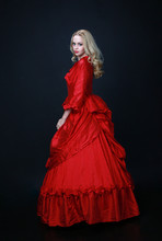 Full Length Portrait Of A Beautiful Blonde Woman Wearing A Historical Red Silk, Victorian Era Ball Gown.
