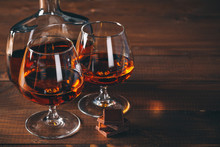 Two Glasses Of Cognac And Bottle On The Wooden Table.