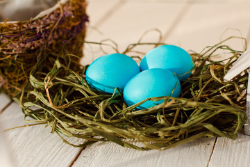 blue Easter eggs in nest on white wooden background