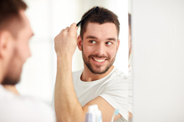 happy man brushing hair with comb at bathroom