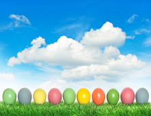Easter Eggs In Green Grass Over Cloudy Blue Sky