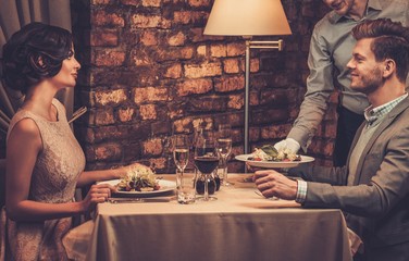 Wall Mural - Waiter serving a plate of salad to stylish wealthy couple in a restaurant.