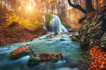 Wall Mural - Beautiful waterfall at mountain river in colorful autumn forest with red and orange leaves at sunset. Nature landscape