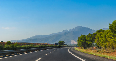 Sunshine on fresh black tarmac on a coastal highway running through the foothills and mountain ranges of continental Europe in Spain.  Road to Madrid.