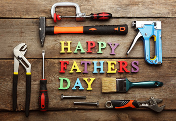 Happy Father's Day inscription with work tools on wooden background. Greetings and presents