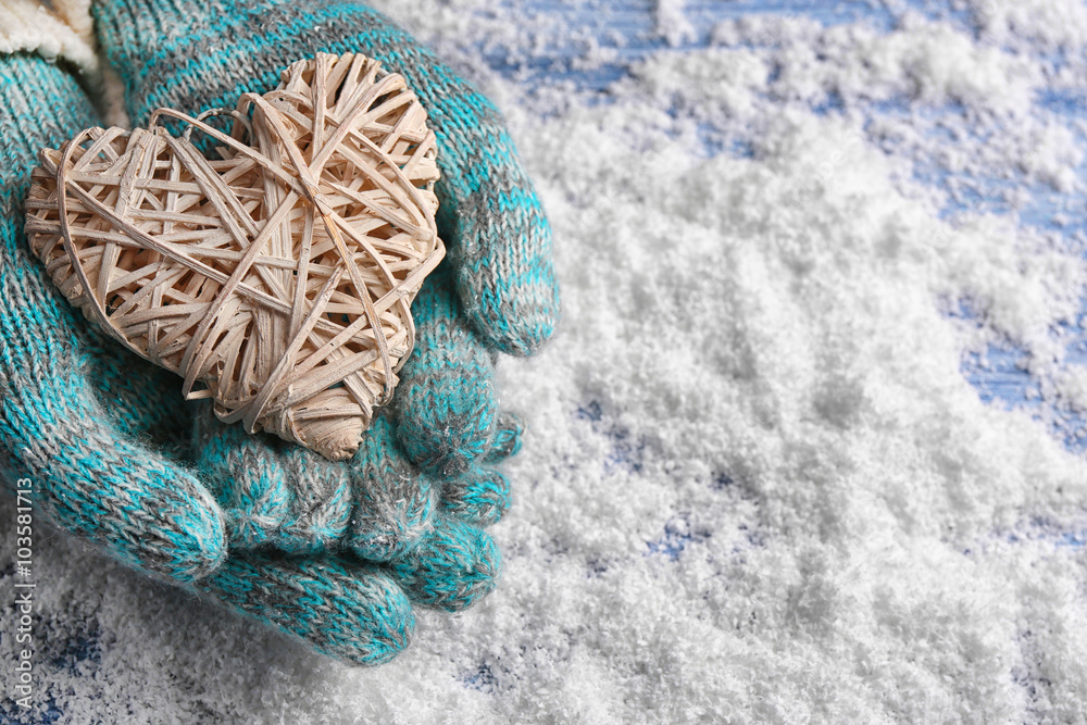 Female hands in mittens with decorative heart on snow background