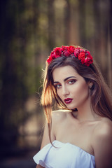 Wall Mural - beautiful young brunette woman in a Park at sunset with flower wreath