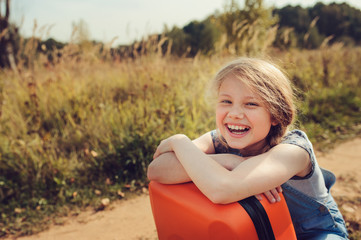 happy child girl with orange suitcase travelling on summer vacation. kid going to countryside. cozy 