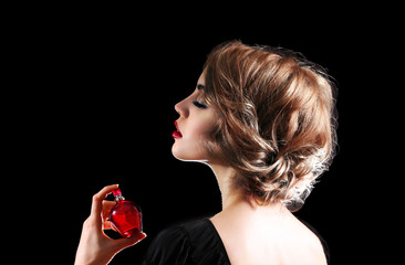 Wall Mural - Beautiful young woman with perfume bottle on black background