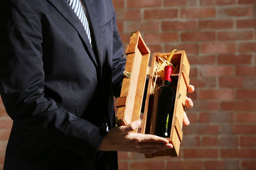 Wall Mural - Man holding a bottle of red wine and glass in wooden box on brick wall background