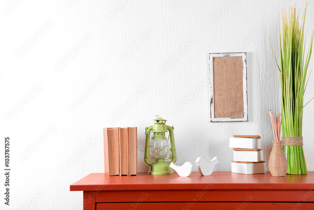 Room interior with red wooden commode, lantern and books on light wall background