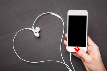 Woman holding smartphone with heart shaped headphones in background 