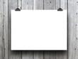 Close-up of one hanged poster paper sheet frame with clips on monochrome wooden boards background