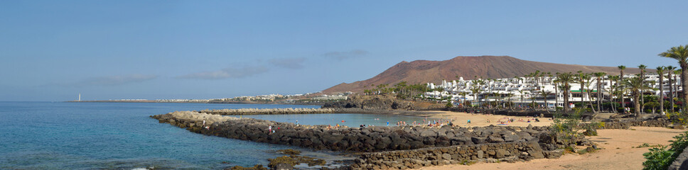  Panorama of the western end of Playa Blanca promenade with holiday makers on the man made Flamingo beach and the lighthouse.