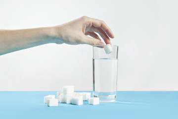 Glass of water against sugar, diabetes disease, sweet addiction, hand drop a sugar