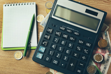 Sticker - Money concept. Black calculator with banknotes and coins on wooden table, close up