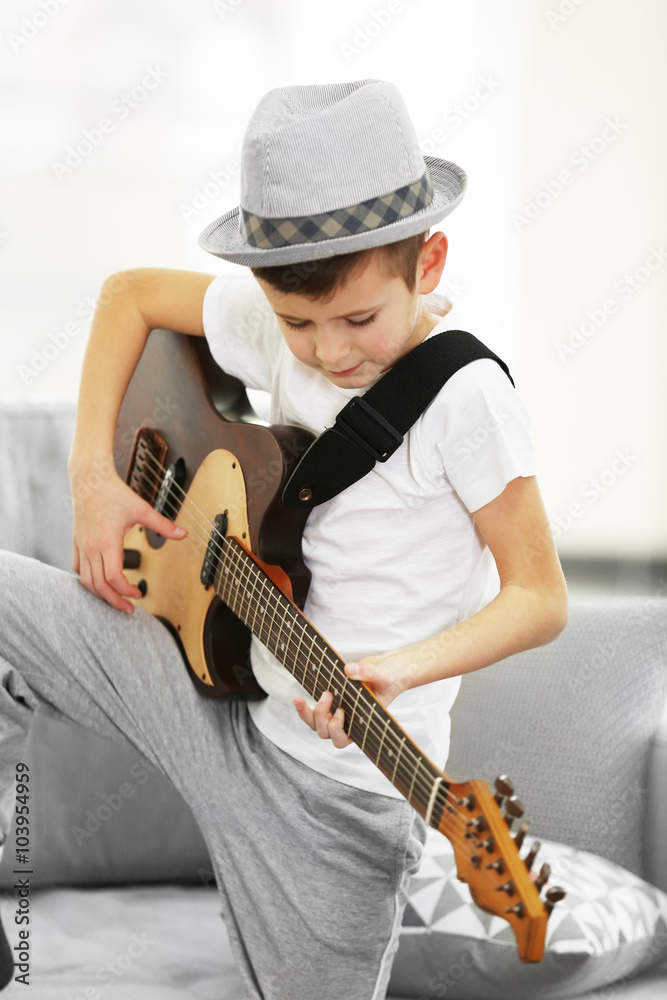 Little boy playing guitar on a sofa at home