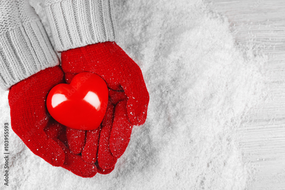 Hands in warm red gloves holding heart on snowy background
