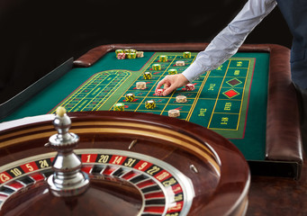 Roulette and piles of gambling chips on a green table. 