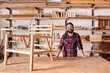 © mavoimages - Smiling craftsman in his woodwork studio with wooden chair frame
